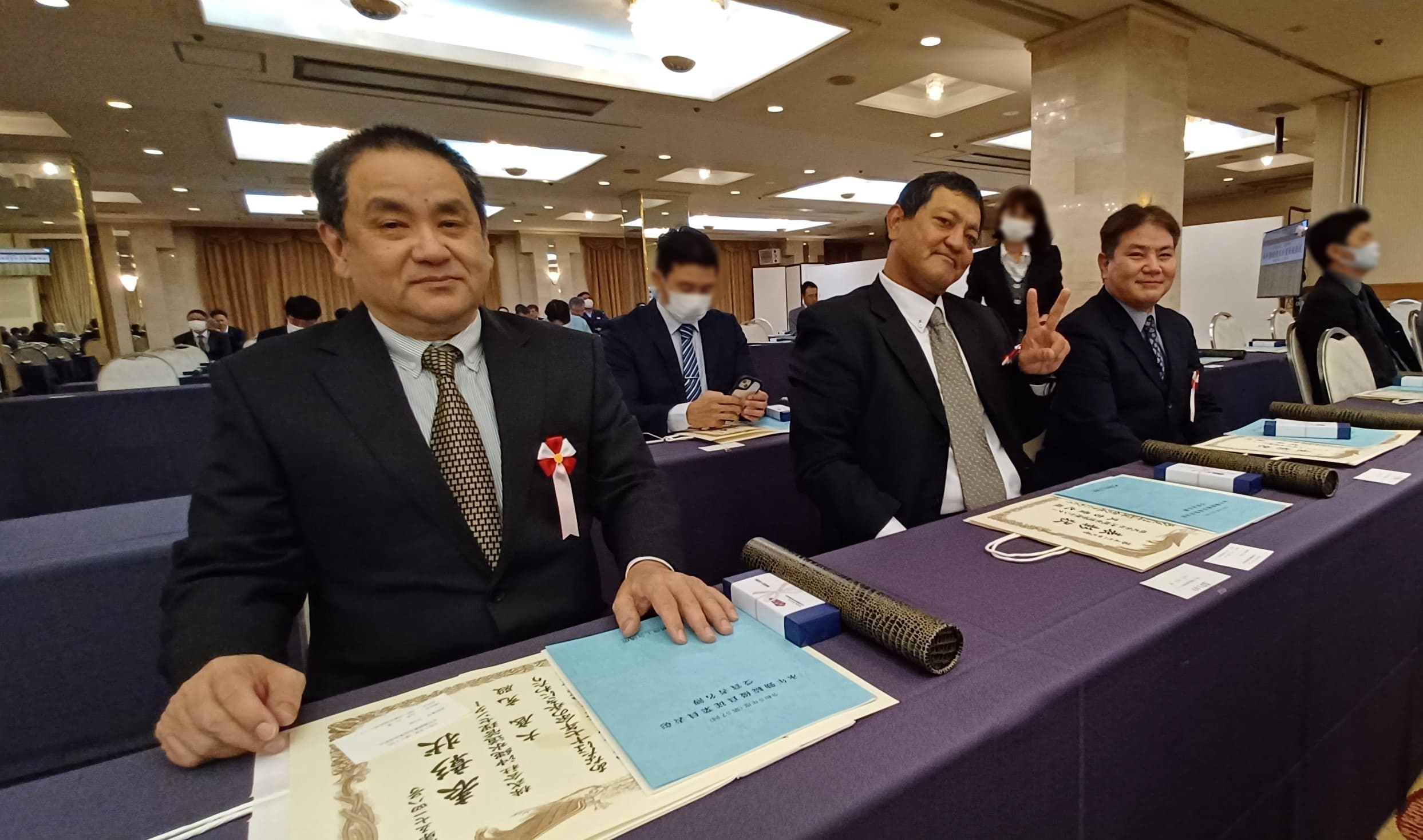 表彰式前に弊社社員3名が並んで座っている写真